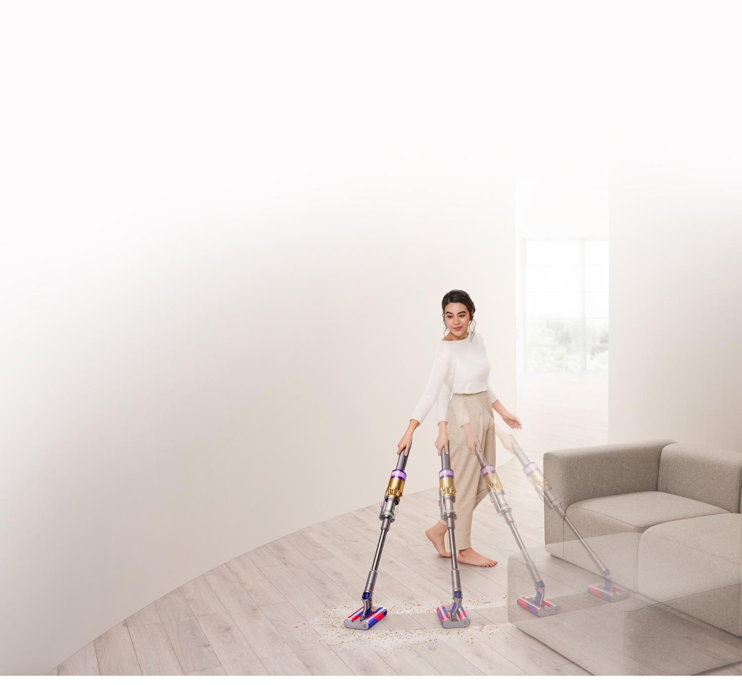 Dyson Omni-glideクリーナーでソファー周りの床を掃除する女性。